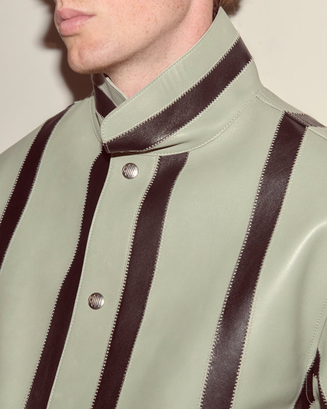 Man wearing the Seafoam Stripe Welding Jacket in seafoam and black, featuring a high collar, wide vertical stripes, and metallic buttons.