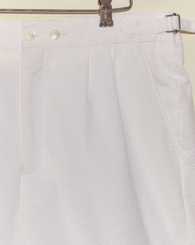 Seersucker Double-Button Shorts with vintage-style side buckle and front buttons hang on a metal hanger against a light background.