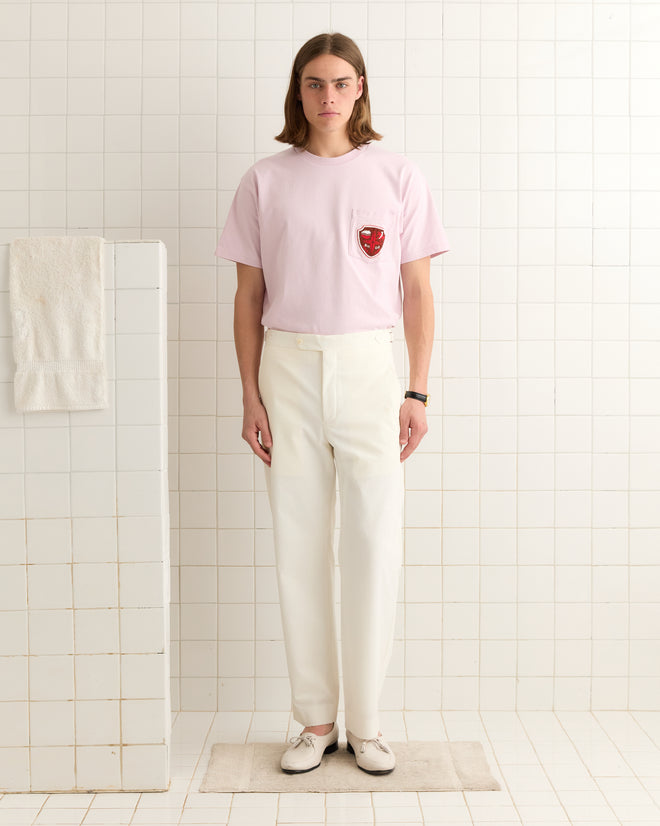 A person in a light pink shirt and mid-rise Seersucker Suiting Trousers stands in a tiled room with pristine white walls, where a towel hangs neatly.