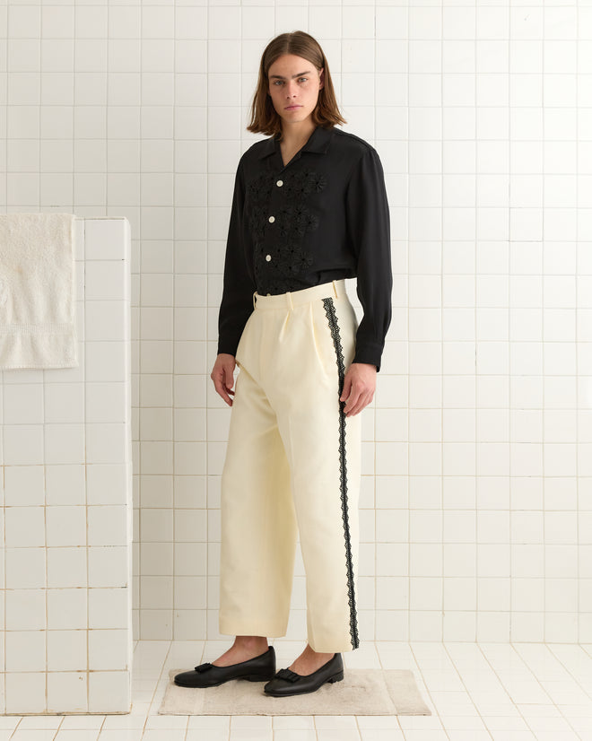A person with long hair in a black shirt and Seymour Suiting Trousers - White stands on a white tiled floor.