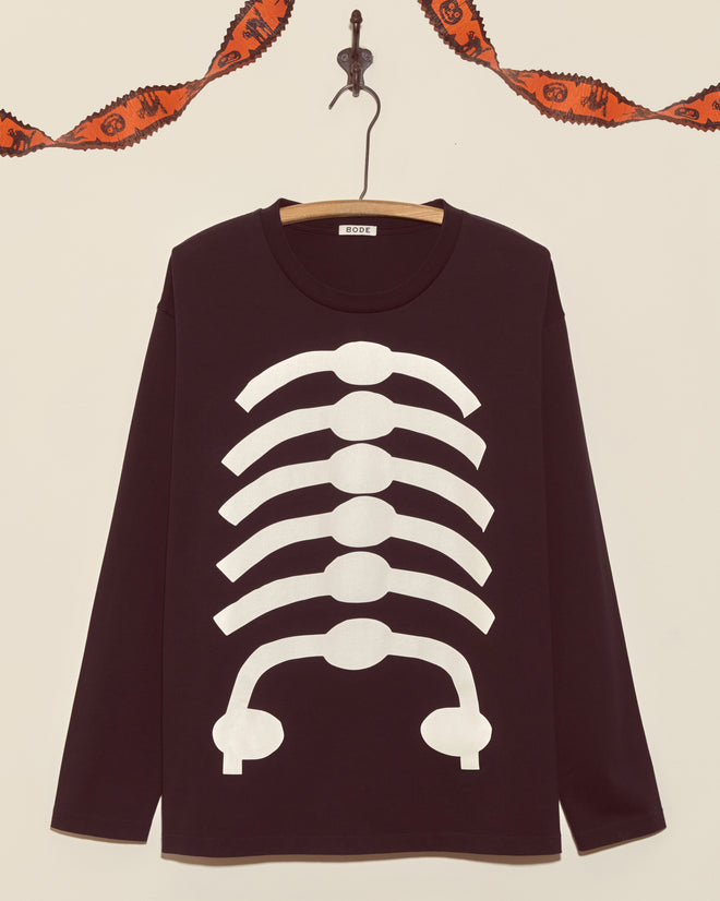 Skeleton Long Sleeve Tee in black with glow-in-the-dark white ribcage print, shown on a hanger with Halloween garland in the background.