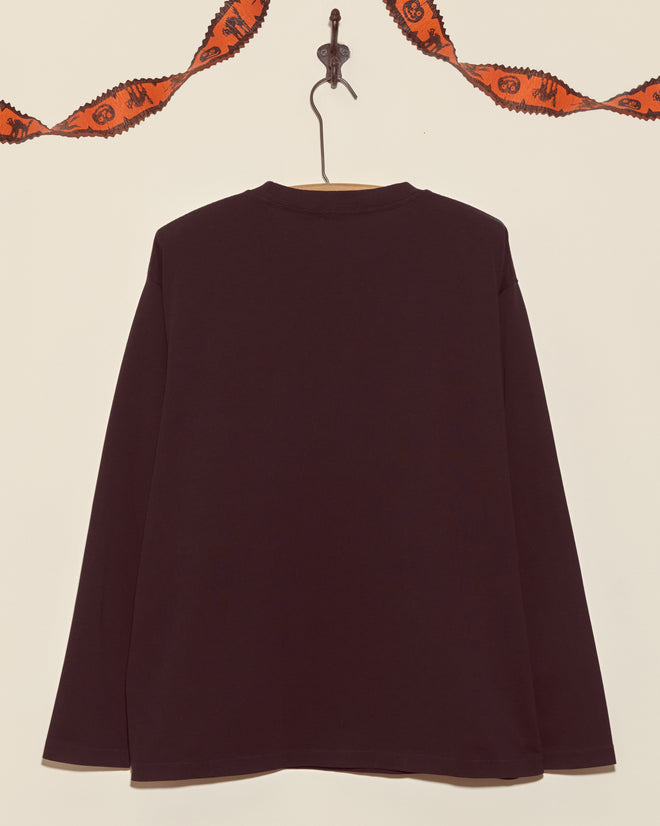 The Skeleton Long Sleeve Tee, a boxy fit black cotton shirt, is displayed on a hook with orange Halloween garland hanging above.