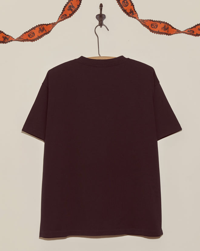 A plain black Halloween shirt on a hanger is displayed against a wall with orange ribbon—this simple style pairs perfectly with your favorite Skeleton Tee for a classic yet festive Halloween look.