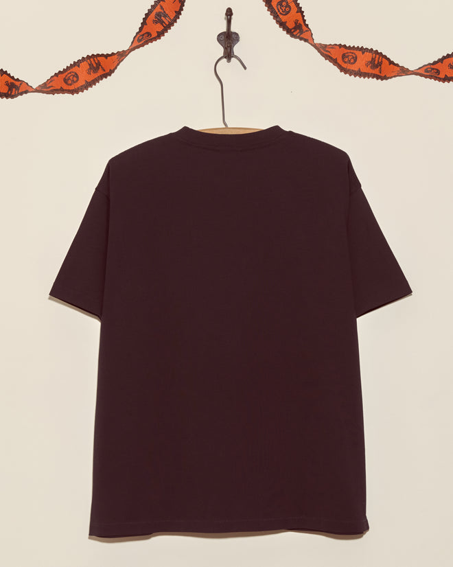A black Skeleton Tee that glows in the dark hangs on a wall with orange festive garland draped above.