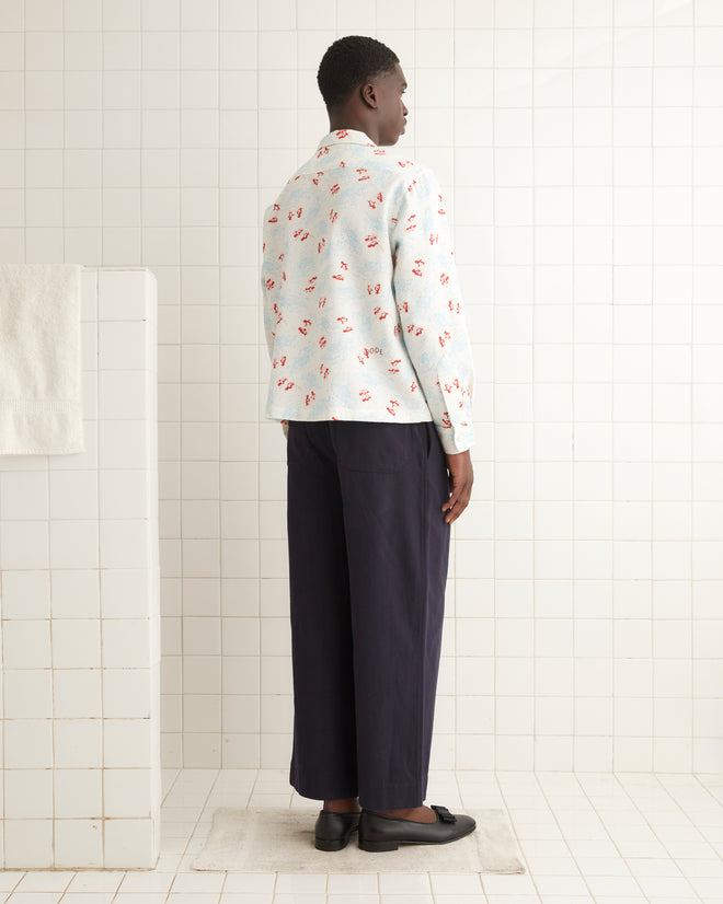 A person in a floral jacket and dark pants stands in a tiled room, their attention captured by patterns akin to a Skiing Penguins Long Sleeve Shirt, adding vintage flair from the 1950s-1960s children's fashion.