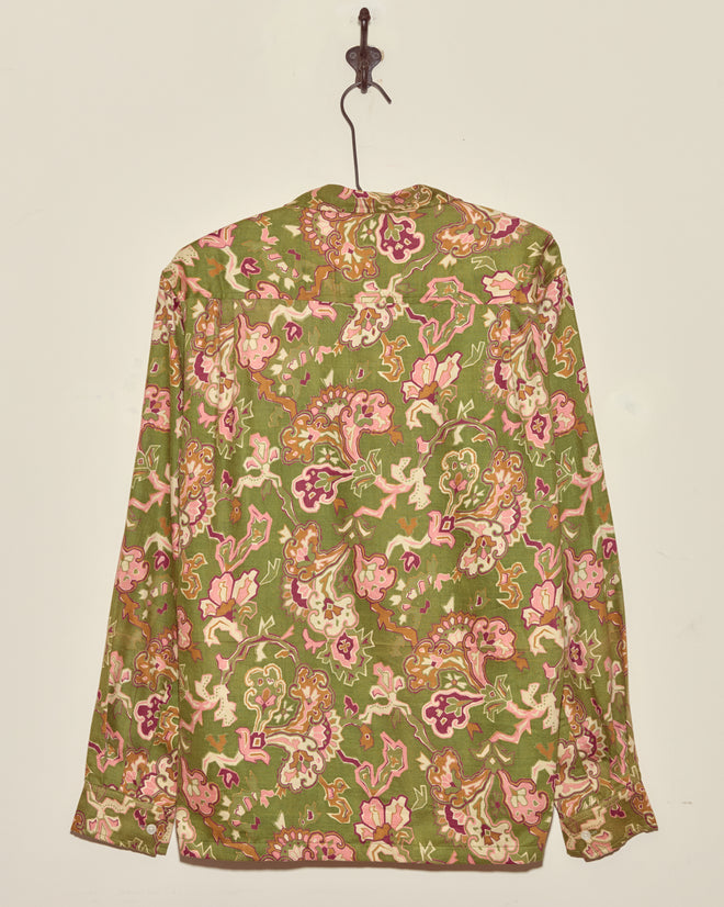 The Smoke Moss Shirt (M/L), a green floral vintage long-sleeve, hangs on a hook against a plain light-colored wall.