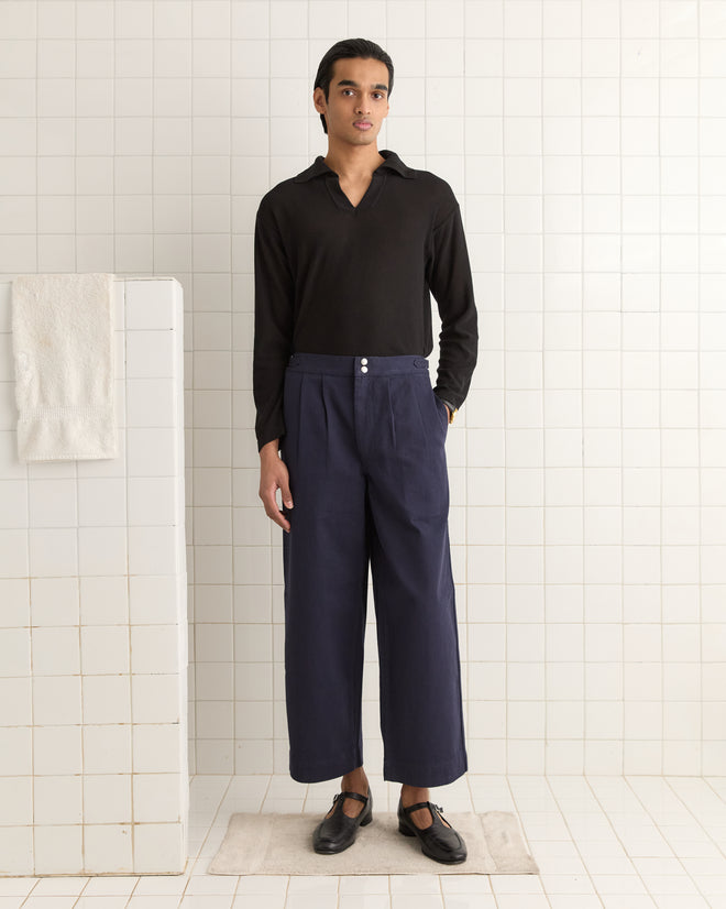A person is in a black shirt and Wide Leg Snap Trousers - Navy, standing on a bath mat in a tiled room.