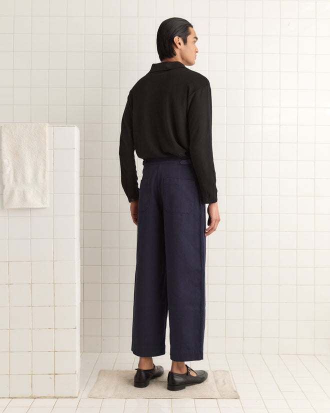 A person in a black shirt and navy Wide Leg Snap Trousers stands on a bathmat in the tiled room, facing away.