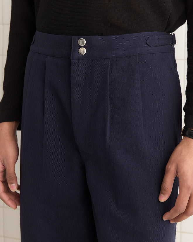 Someone wearing Wide Leg Snap Trousers in navy, inspired by vintage Australian military style, paired with a black shirt. The look is completed with metal buttons and side buckle waist adjusters, highlighting the classic heavyweight twill fabric.