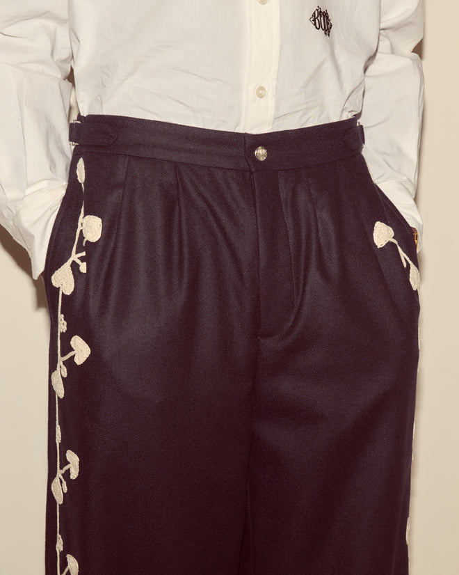 Person wearing the Snowdrop Appliqué Trousers in navy, featuring white floral appliqué on the sides, paired with a white button-up shirt.