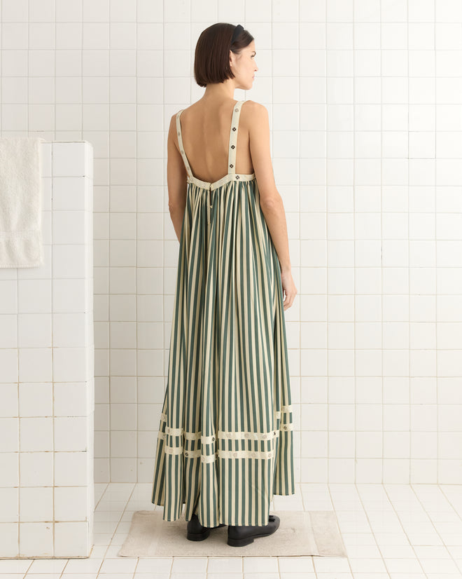 Standing in a tiled room, with a towel to the left, one wears the Soda Stripe Dress, inspired by 1940s design, featuring green and white silk stripes.