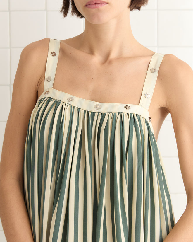 A person models the Soda Stripe Dress, featuring a 1940s-inspired design with grey-green stripes and floral details, standing elegantly against a tiled backdrop.