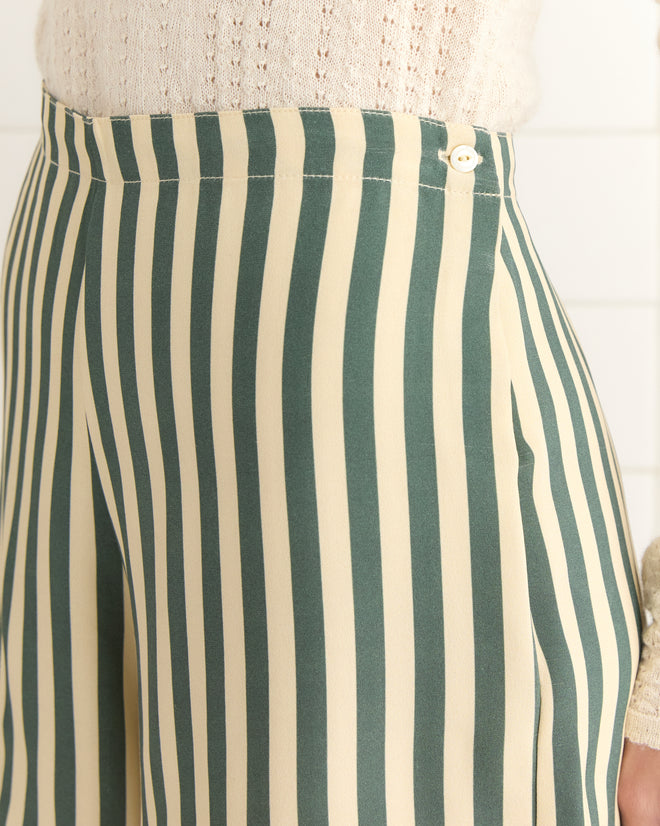 Close-up of Soda Stripe Shorts in green and cream vertical stripes with antique pearl buttons, paired with a light knitted sweater.