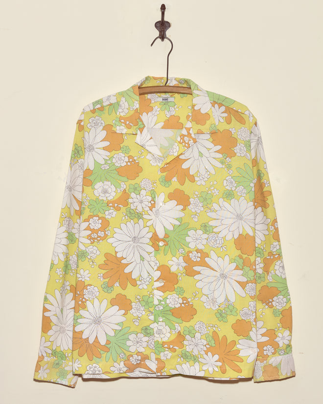 The Storytime Floral Shirt (XL/XXL), crafted from a vintage yellow, orange, and white floral bedsheet, hangs on a hanger.
