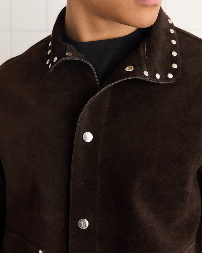 A person wearing the Studded Welding Jacket - Brown, featuring dark suede material with silver studs on the collar and metal snap buttons.
