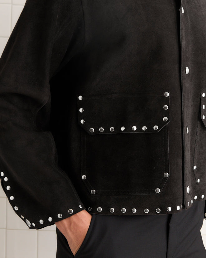 A person wearing the Studded Welding Jacket - Black, featuring silver studs on the pockets, cuffs, and hem, exuding a bold, specialist style.