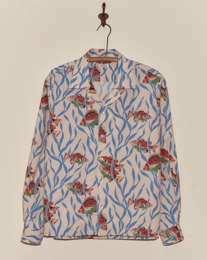 The Swimmers Long Sleeve Shirt features a colorful fish pattern on blue seaweed crepe fabric and hangs neatly on a hook.