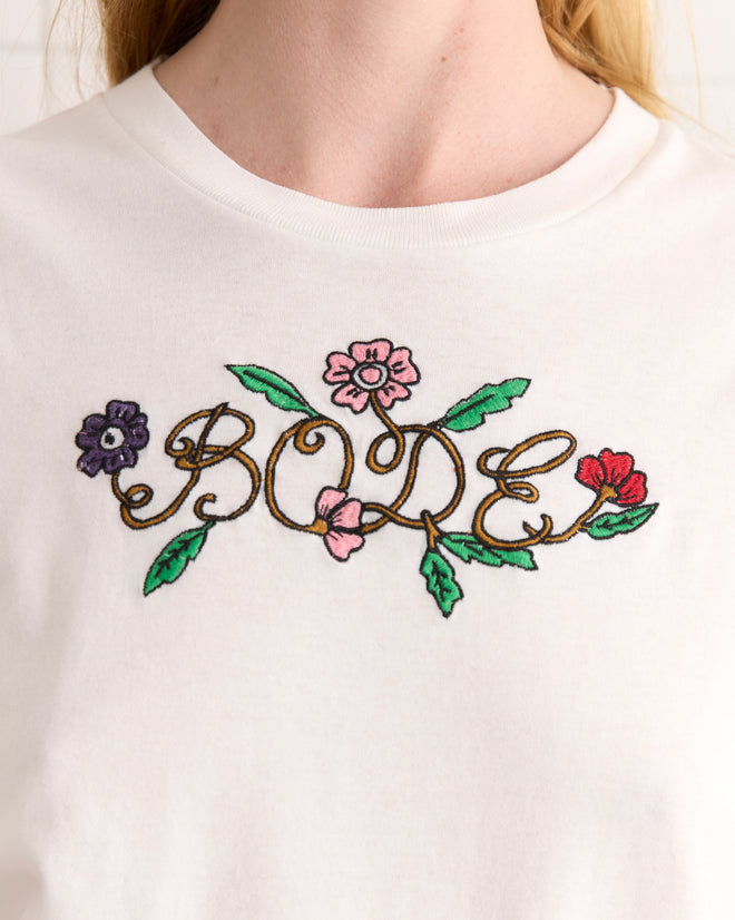 The Posy Tee is a white shirt made from 100% cotton, showcasing a vibrant floral pattern that spells