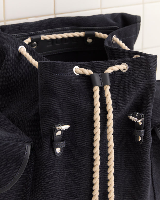 Close-up of the Canvas Rucksack - Black, made from heavyweight canvas with cream rope drawstrings and leather accents for style and durability.