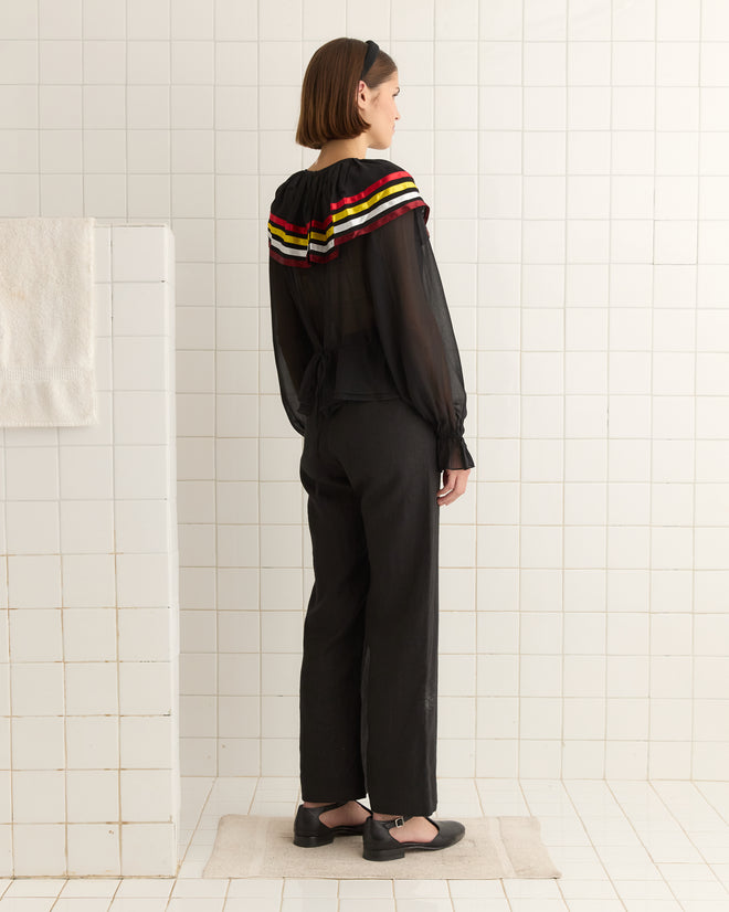 A person wearing the Talo Ruffle Top in Black/Multi stands facing away in a tiled room.