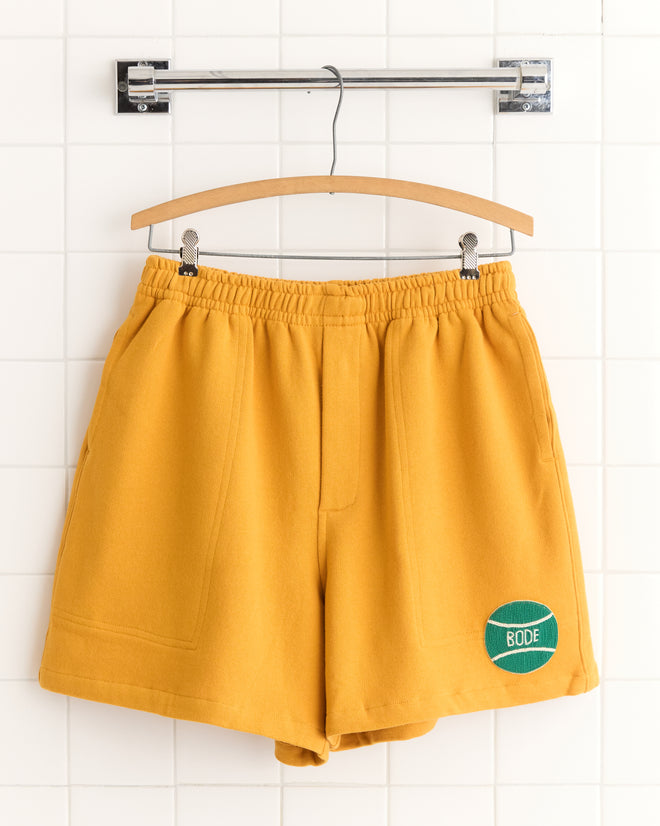 Mustard yellow cotton Tennis Ball Patch Shorts with an elastic waistband and a green
