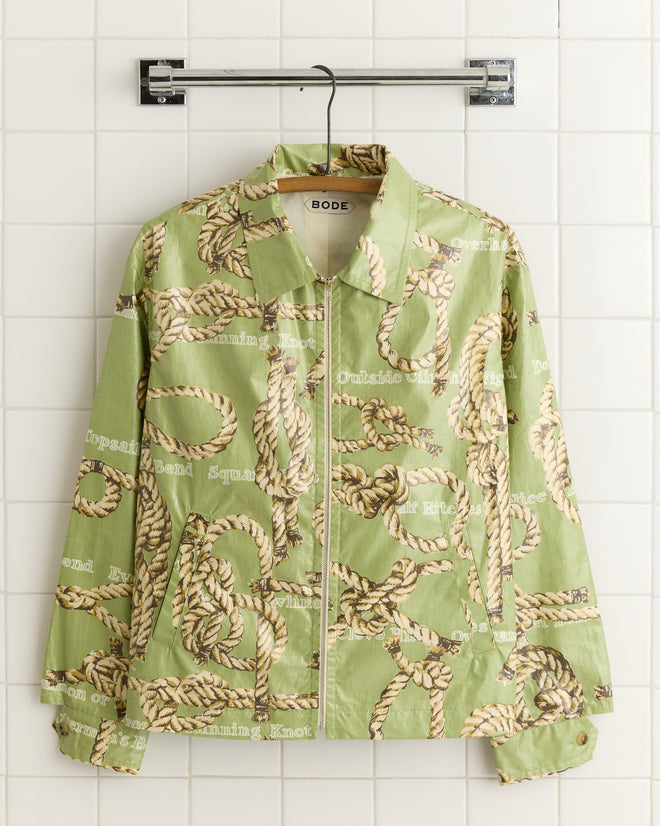 A Topsail Rope Jacket, featuring a sailor's knots pattern in green, hangs on a white tiled wall.