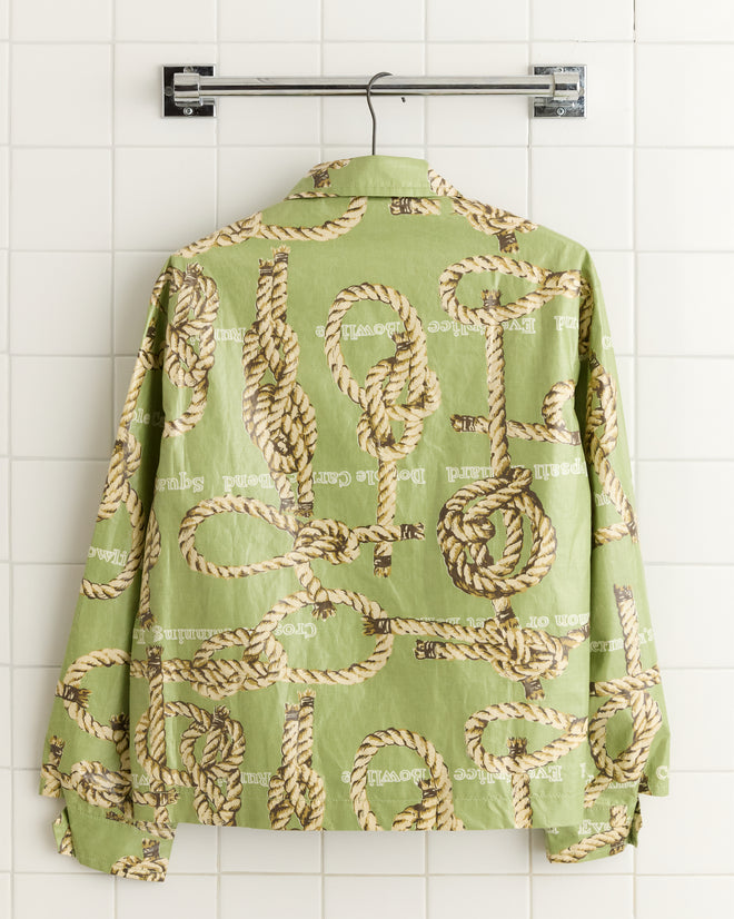 The Topsail Rope Jacket, featuring a charming rope design similar to sailor's knots, elegantly hangs on a white tiled wall.