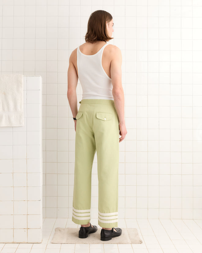 A person in a white tank top and Tri-Stripe Trousers in Green/Cream stands in a tiled room, facing away.