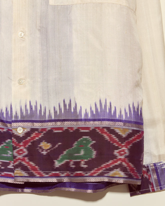 The Turaco Silk Shirt - L/XL showcases a white base with a purple and green patterned border and bold jagged purple detail above the hem. Crafted from silk and made in New York, it's a unique statement piece.
