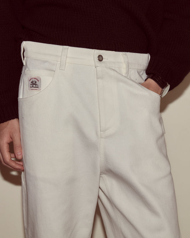 A person is facing the camera, wearing white Twill Knolly Brook Trousers from Bode and a dark sweater, with one hand in their pocket.