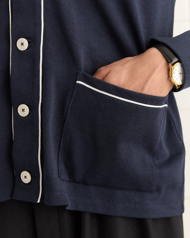 A person is wearing the Uniform Cardigan in dark blue, featuring white buttons and trim, crafted from heavyweight fabric, with one hand resting in a pocket.