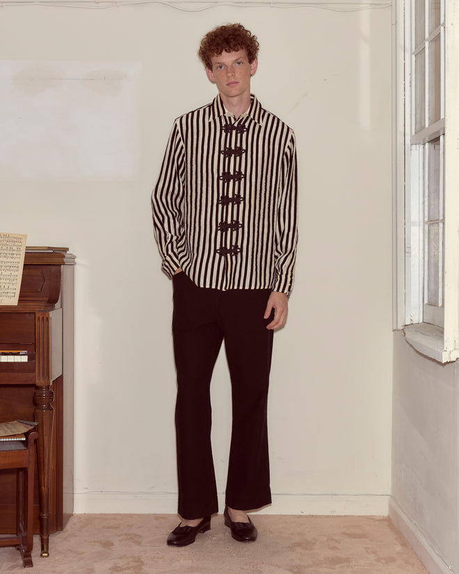 A person wearing the Velvet Bannister Shirt and black pants stands beside a piano in a brightly lit room.