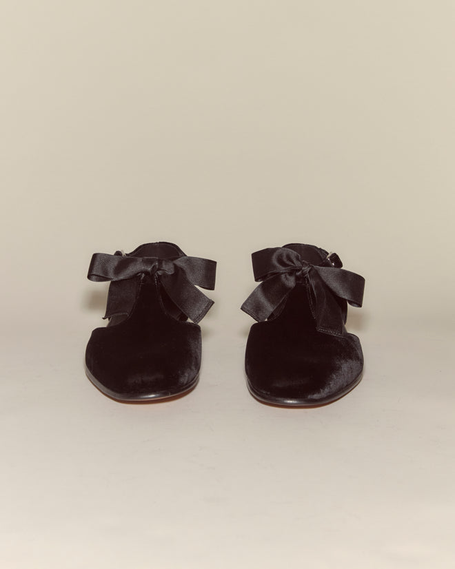 The Velvet Theater Shoes - Black feature large ribbon bows and a classic T-strap, crafted in soft black velvet and shown against a plain background.