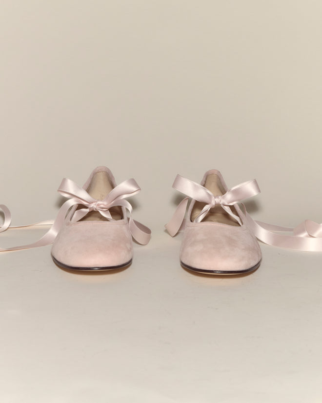 Musette Flats - Pink: A pair of pale pink suede ballet flats with ribbon laces, arranged side by side on a simple light background.