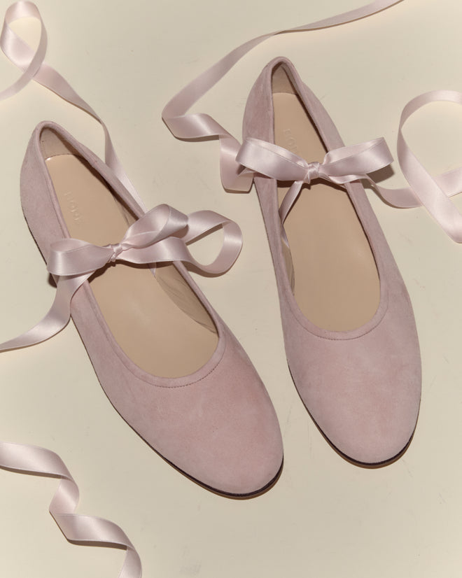 Musette Flats - Pink: Chic pink suede ballet shoes with pale pink ribbon laces, styled on a light surface for a vintage-inspired look.