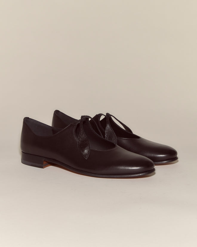 The Verbena Shoes - Black are Italian-made leather Mary Janes featuring decorative cutouts and bows, shown on a plain background.