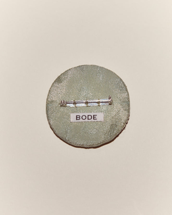 The Willow Brooch - Green is a round satin pin with a metal clasp and a “BODE” label, showcased on a plain background—an elegant Bode accessory.