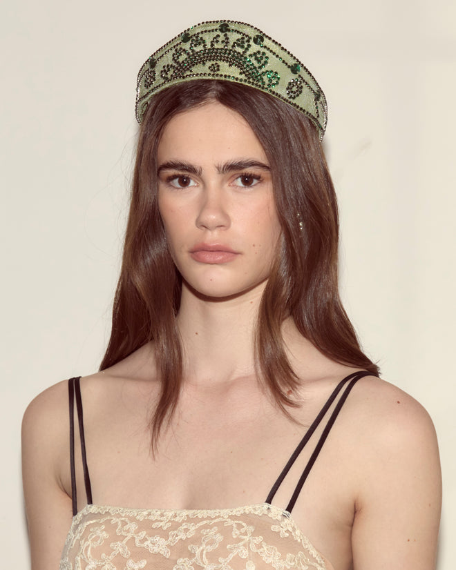 Woman with long brown hair wearing the Willow Crown - Green, styled in a 1930s jeweled design, and a lace dress with thin black straps.