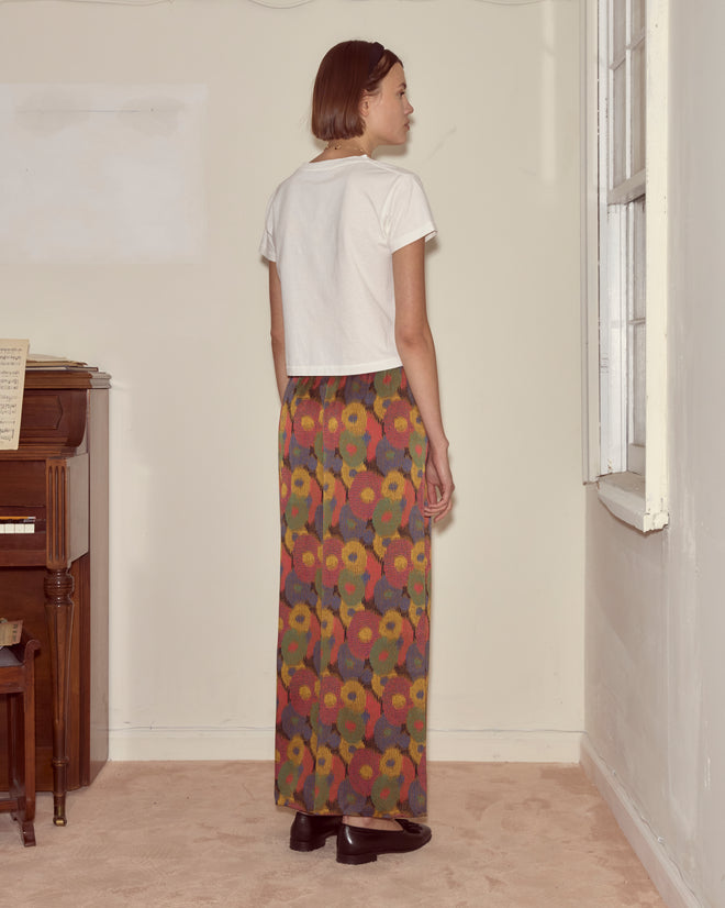 A woman with short hair stands by a window, wearing a white shirt and the Fruit Pit Pants—wide-leg silk seersucker trousers.