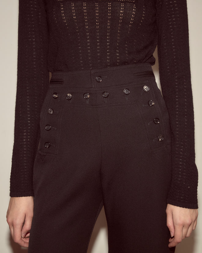 Person wearing a black knit top and Riding Twill Sailor Trousers - Black, featuring high-waisted styling with decorative front buttons.