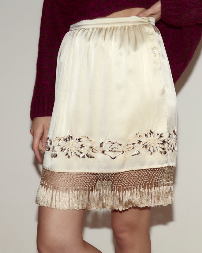 A person faces forward wearing the Phantasm Fringe Skirt in ivory silk with Victorian embroidery and a fringe hem, paired with a purple sweater.