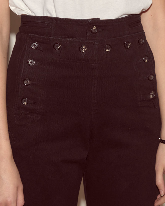 Someone wearing the Denim Sailor Trousers - Black, featuring a high-waisted fit with multiple buttons, paired with a tucked-in white shirt.