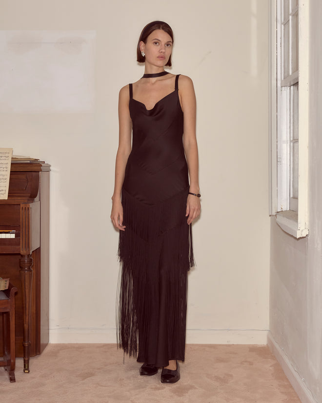 Woman wearing the Tango Fringe Dress stands indoors by a piano and window, looking at the camera.