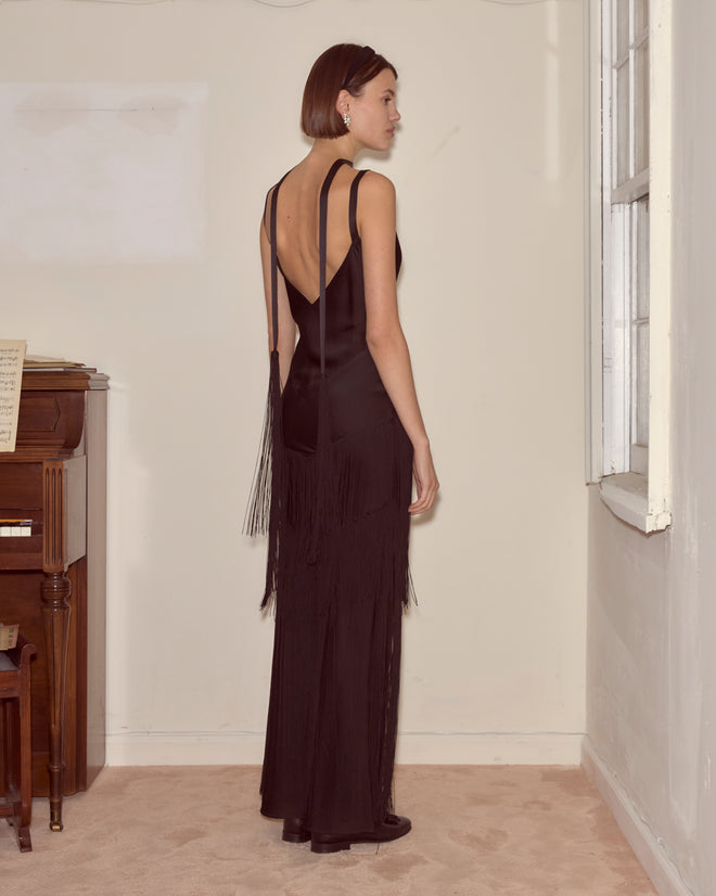 A woman in a Tango Fringe Dress stands near a window, facing away, in a room with a piano.