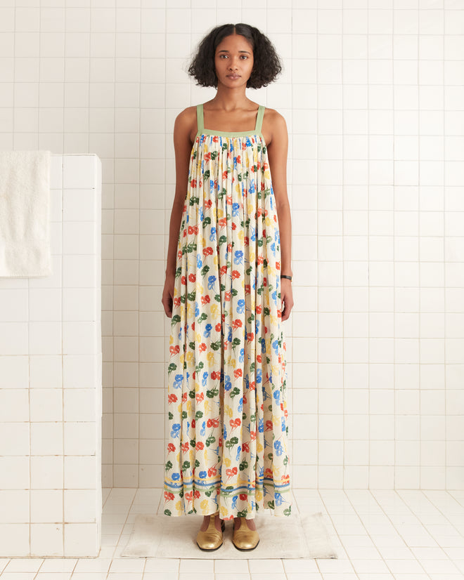 In a vintage-style Flower Stamp Dress made of 100% cotton, someone stands on a white tiled floor, with a towel hanging on a rack to the left.