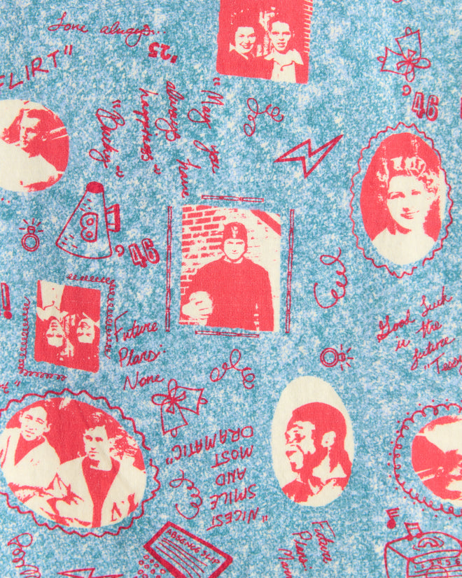 The Yearbook Tee features red vintage-style illustrations and text on a blue textured background, reminiscent of printed fabric, with various people and symbols.
