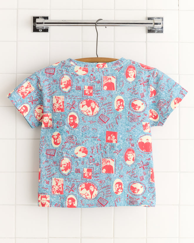 The Yearbook Tee, a vibrant cotton T-shirt adorned with vintage celebrity portraits and playful icons, hangs gracefully against a tiled wall, capturing the nostalgic charm of the 1950s-1960s.