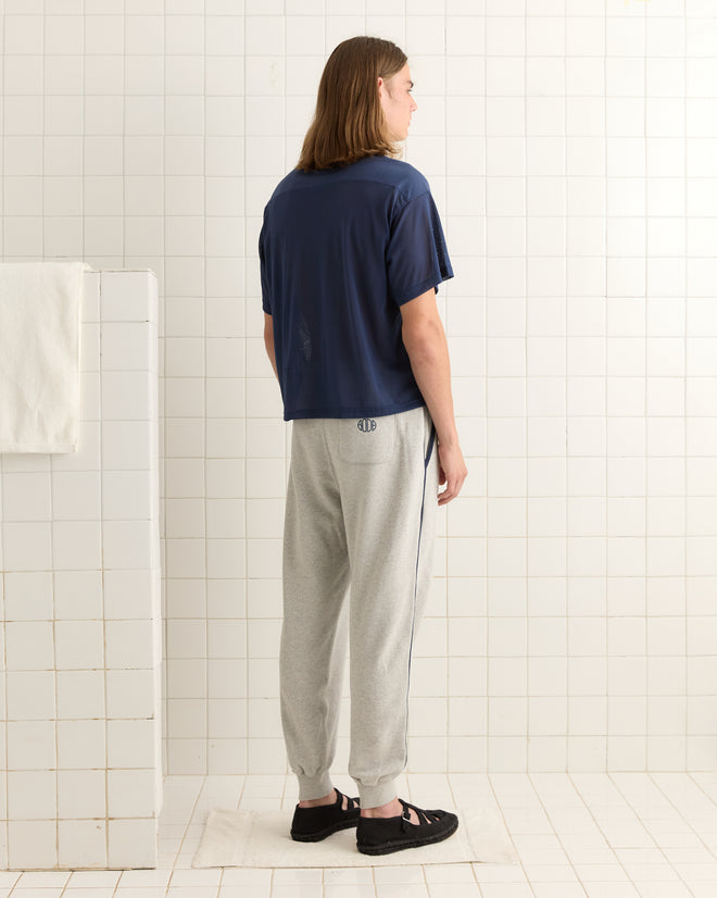 A person stands in a tiled room, facing away, wearing the Scrimmage Jersey - Navy, gray sweatpants, and black sandals.