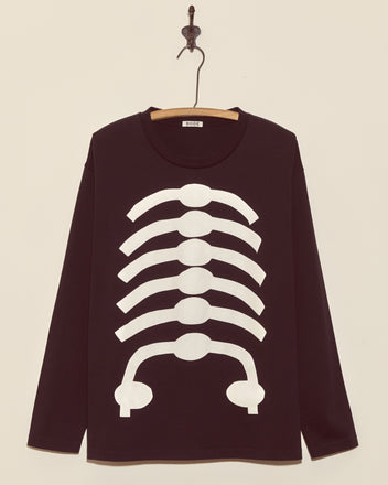 The Skeleton Long Sleeve Tee is a black shirt with a white ribcage graphic, displayed on a wooden hanger against a cream wall. This vintage tee features a boxy fit, making it perfect for your spooky season style.