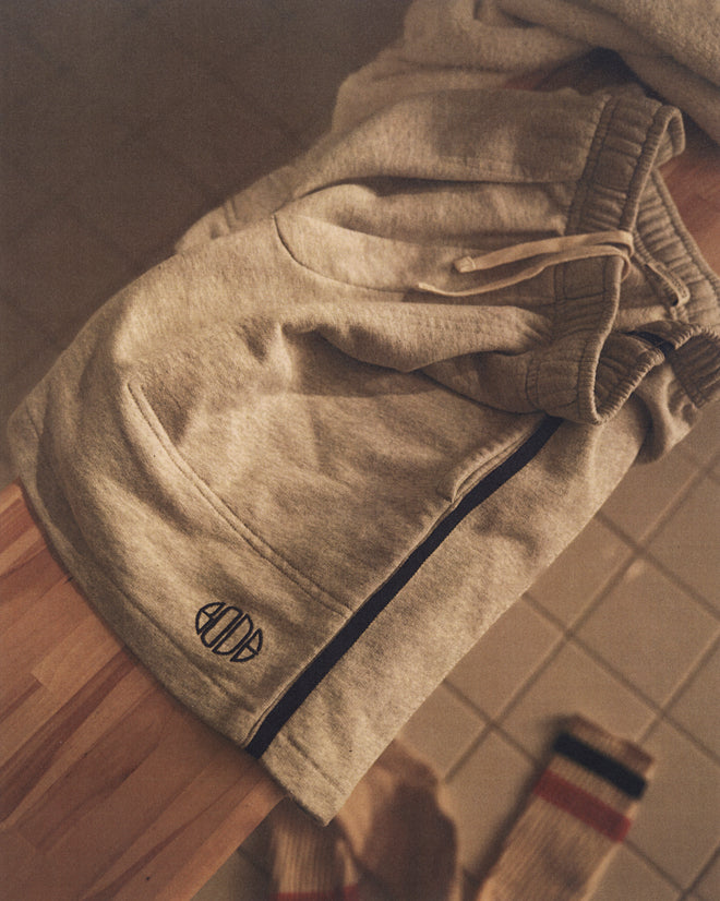 Crew Sweatshorts - Heathered Grey, featuring a drawstring and small black logo, folded on a wooden surface beside socks on a tiled floor.